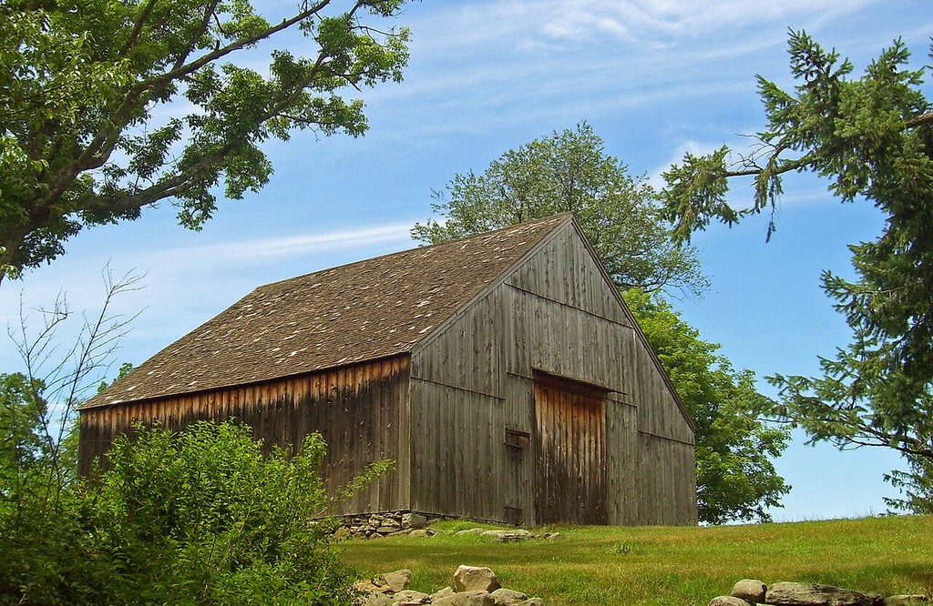 A broad gabled timber barn has large central wagon doors and weatherboarded walls.