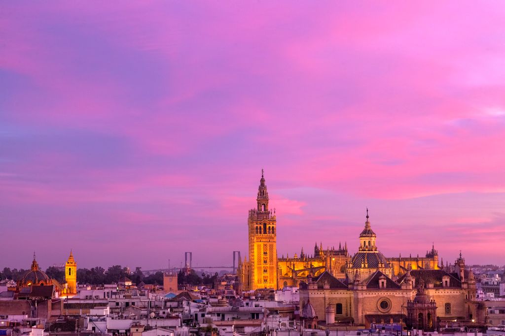 Seville's skyline at magenta sunset, with the tall Giralda tower beside the cathedral and low city roofs.