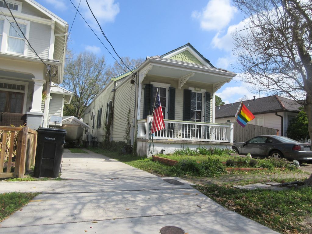 A narrow pale-green timber house has a small gabled porch and a long side wall with repeated windows extending behind the street front.