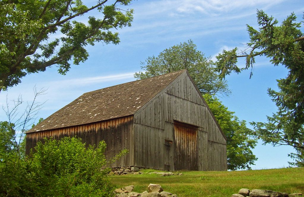 A broad gabled timber barn has large central wagon doors and smaller side doors.