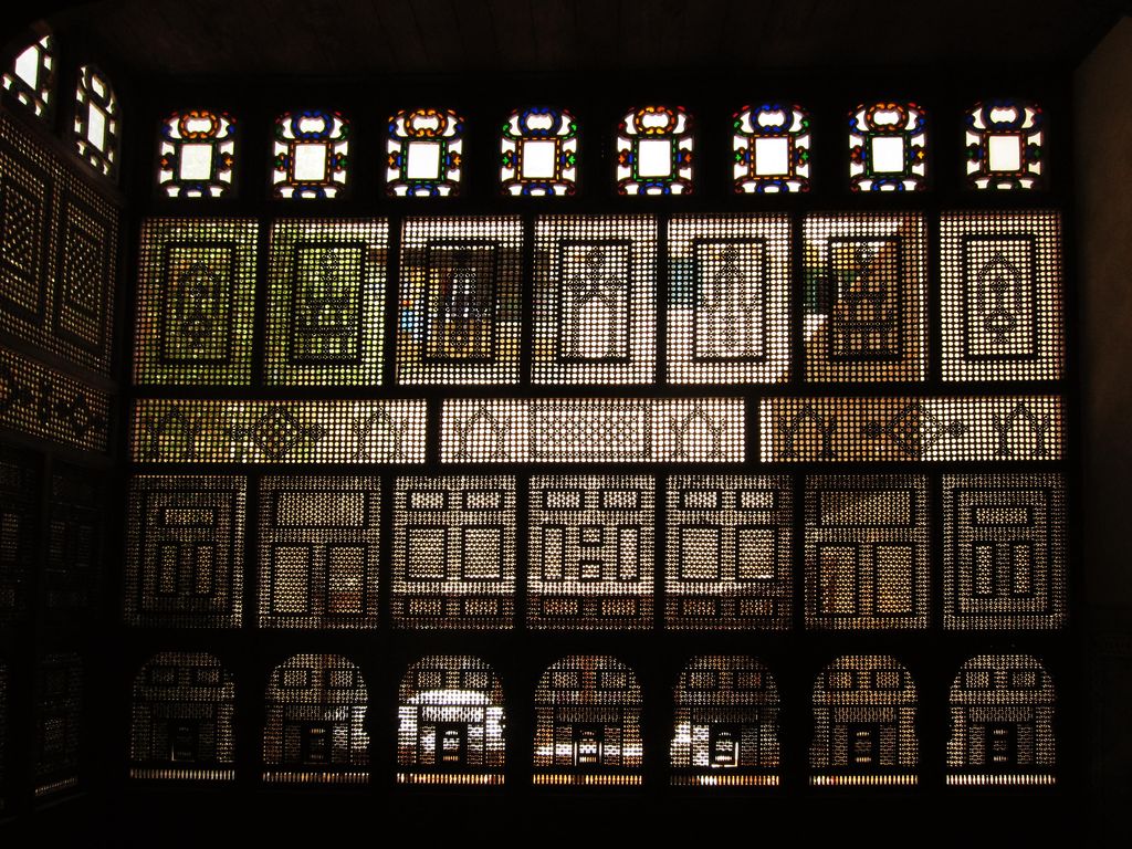 Dark timber lattice screens glow with many small geometric openings and a row of coloured glass above.