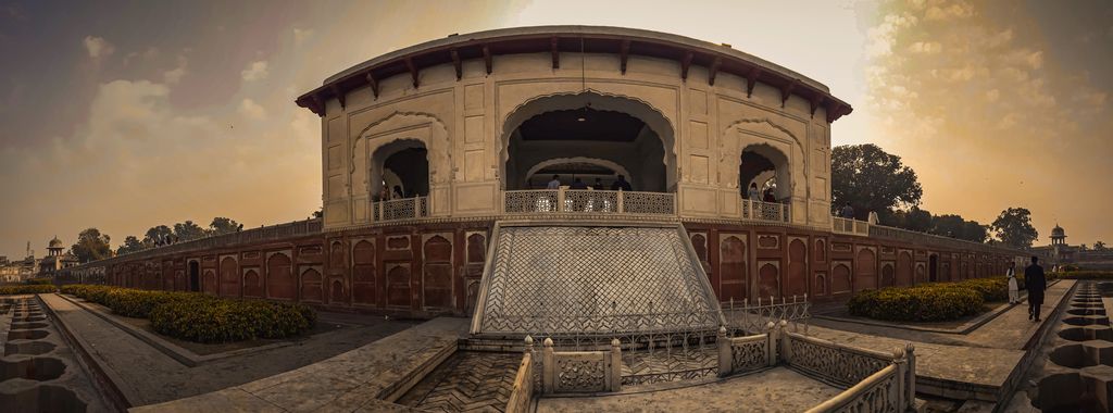 A very wide view shows an octagonal pavilion beyond a large dry basin, low red walls, gardens and trees at sunset.