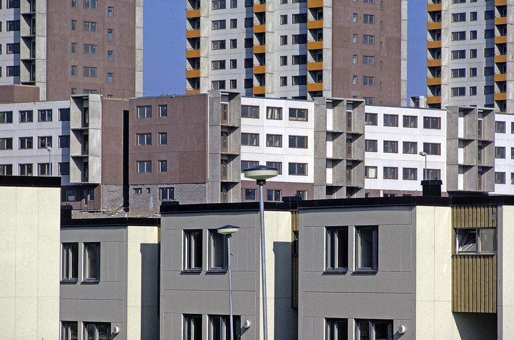 Low grey housing fills the foreground, with long mid-rise blocks and tall pink and white apartment towers rising closely behind.