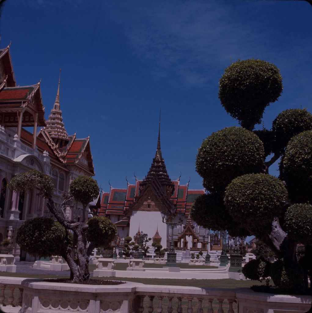 A slightly dark historical colour view shows palace buildings with peaked roofs, pale façades and clipped trees around a formal courtyard.