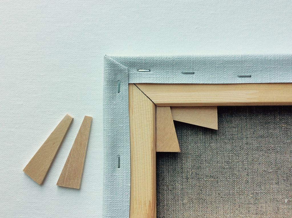 Rear corner of a stretched canvas showing fabric, staples, wooden bars and two loose wooden keys.