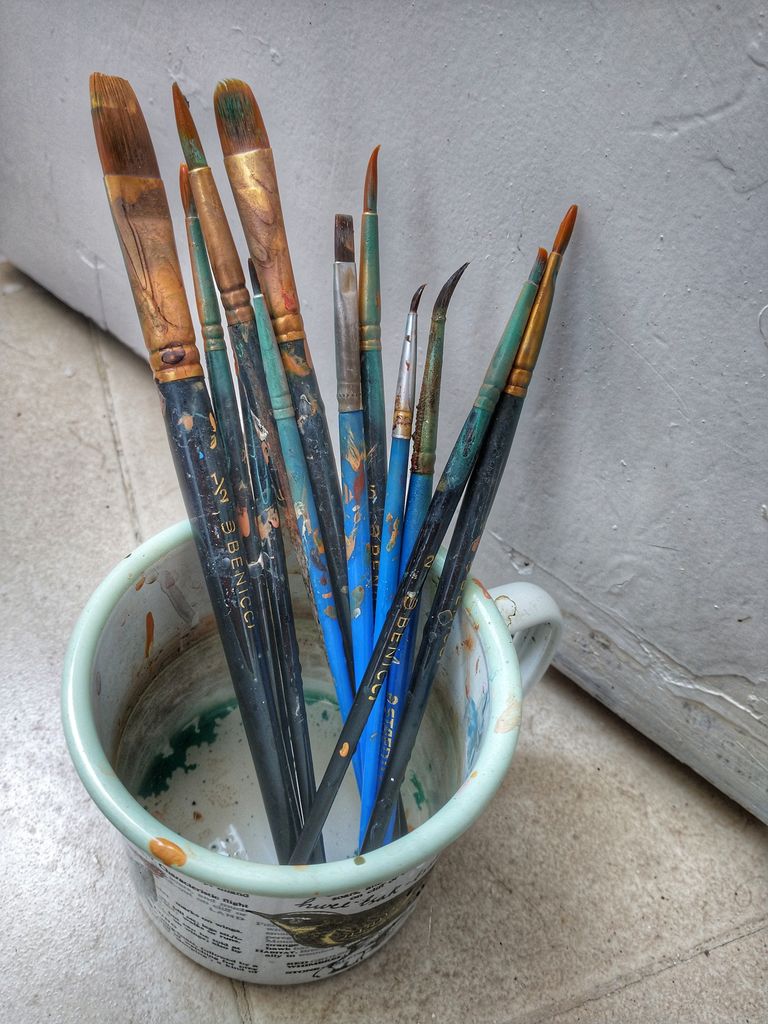 Used paintbrushes standing in a container with stained ferrules, handles and bristles.