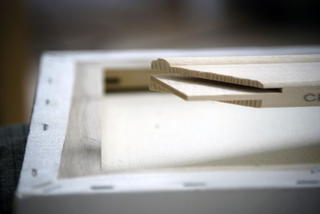 Side profile of a wooden stretcher bar with a raised lip beneath stretched canvas.
