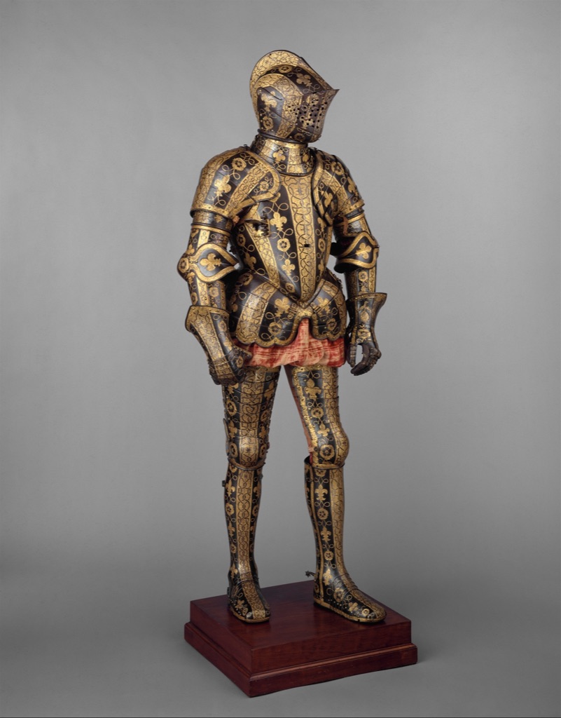 The Clifford armour garniture stands as a complete suit with dark steel, gold decoration, perforated visor, articulated plates and red textile visible beneath.