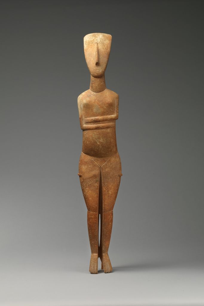 A slender marble female figure stands with a small tilted head, folded arms, long torso and joined legs.