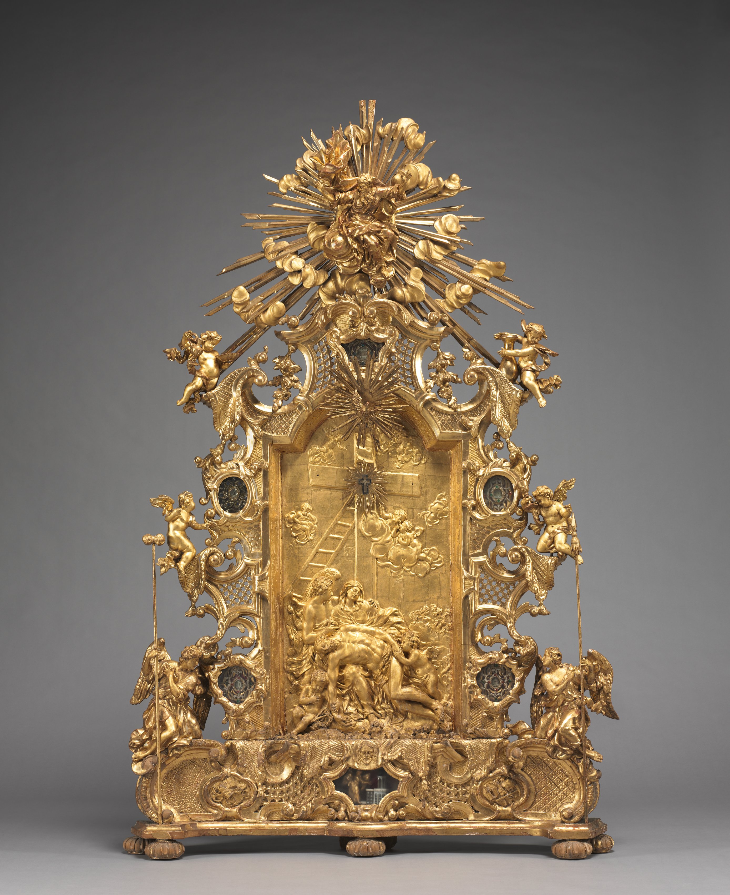 Tall gilded Bavarian altarpiece crowded with relief scenes, rays, scrolls, angels and relic niches incorporating gold wire.